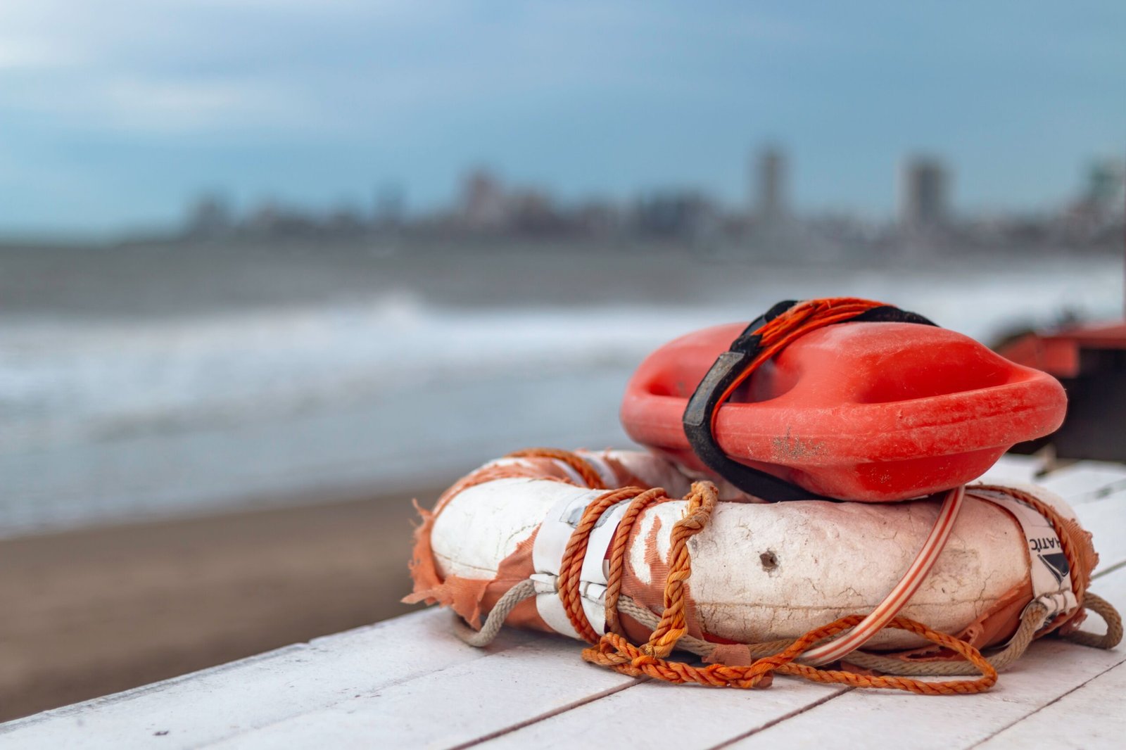 Close-up of a lifebuoy and rescue float on Mar del Plata beach in Argentina, with city skyline in the background.