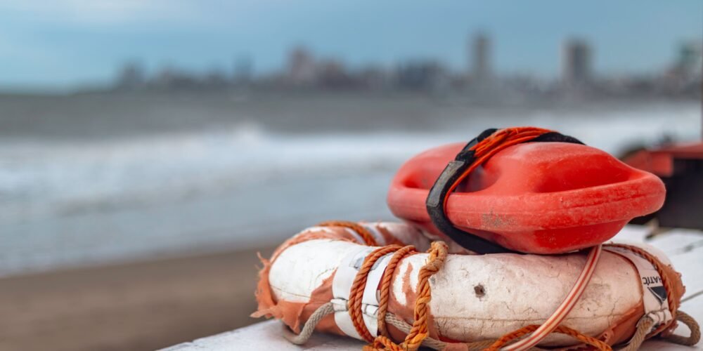 Close-up of a lifebuoy and rescue float on Mar del Plata beach in Argentina, with city skyline in the background.